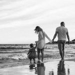 A family enjoys a peaceful walk along the beach with gentle waves.