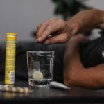Elderly man lays in bed while dissolving a soluble medicine in water, indicating health and wellness home care.