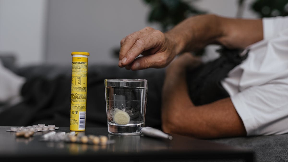 Elderly man lays in bed while dissolving a soluble medicine in water, indicating health and wellness home care.